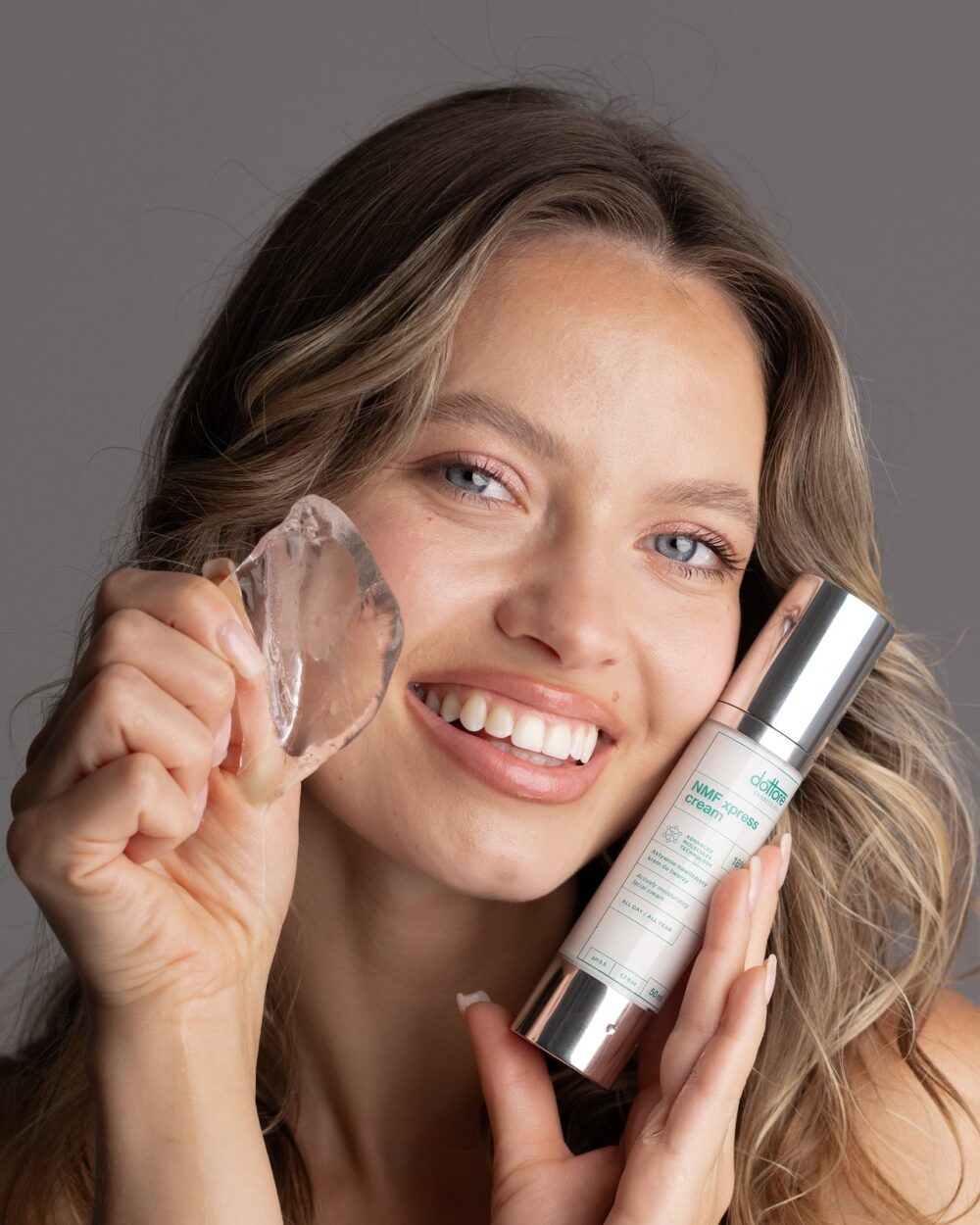 Uśmiechnięta modelka z NMF xpress cream i bryłą lodu przy twarzy