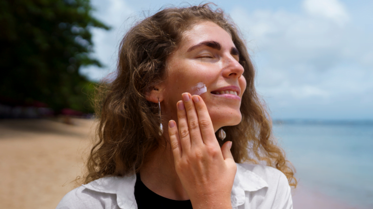 Kobieta na słonecznej plaży nakłada krem z filtrem SPF na twarz