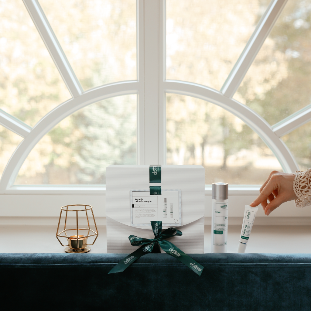 Dłoń sięgająca po tubkę kremu pod oczy z zestawu prezentowego z retinolem stojącego na oknie