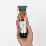 Dłoń trzymająca srebrną tubkę peelingu enzymatycznego z grafiką papai na białym tle