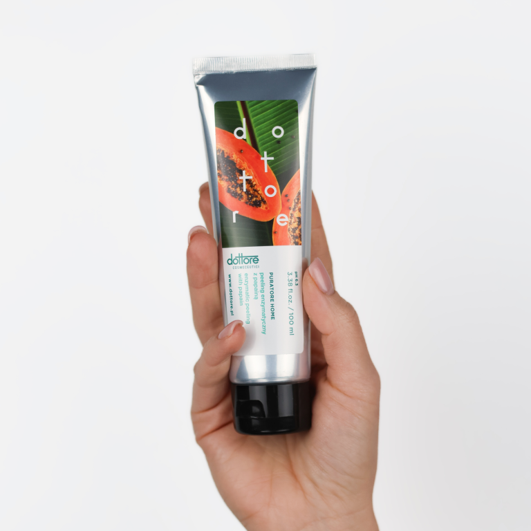 Dłoń trzymająca srebrną tubkę peelingu enzymatycznego z grafiką papai na białym tle