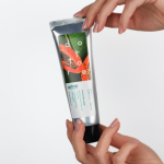 Kobiece dłonie trzymające tubkę naturalnego peelingu enzymatycznego na białym tle