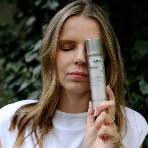 Kobieta z zamkniętymi oczami trzymająca przy twarzy butelkę kremu nawilżającego Hydratore na tle zieleni