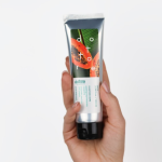 Dłoń trzymająca srebrną tubkę peelingu enzymatycznego z grafiką papai na białym tle