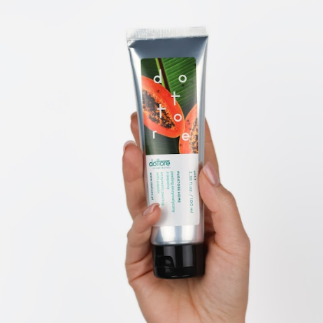 Dłoń trzymająca srebrną tubkę peelingu enzymatycznego z grafiką papai na białym tle