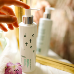 Delikatny płyn micelarny dla skóry wrażliwej stojący przy lustrze obok fioletowego kwiata.