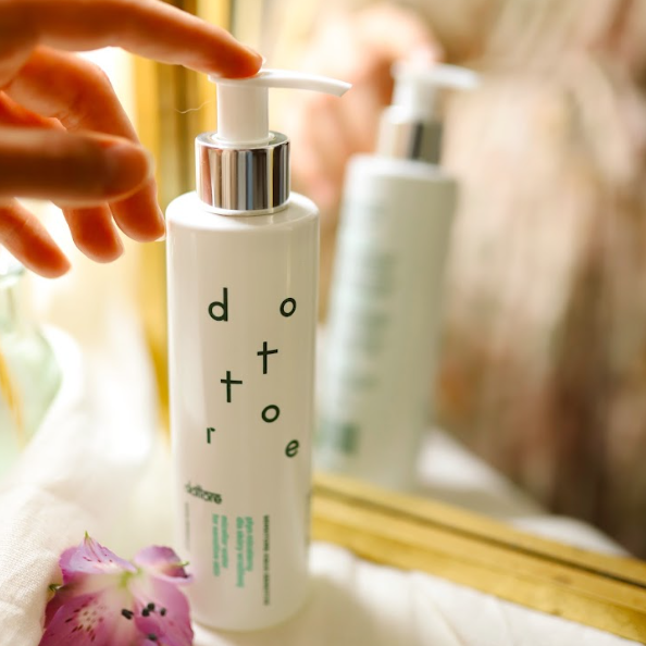 Delikatny płyn micelarny dla skóry wrażliwej stojący przy lustrze obok fioletowego kwiata.