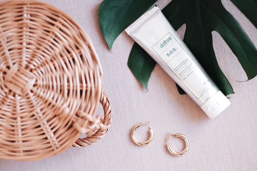 Regenerujący krem SOS w tubce leżący na jasnym tle w otoczeniu kobiecych dodatków.