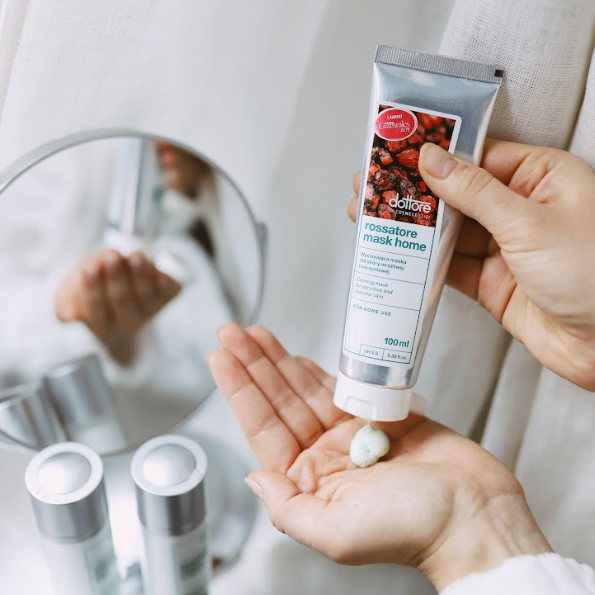 Dłonie wyciskające kremową maseczkę do twarzy z tubki przed nałożeniem na skórę.