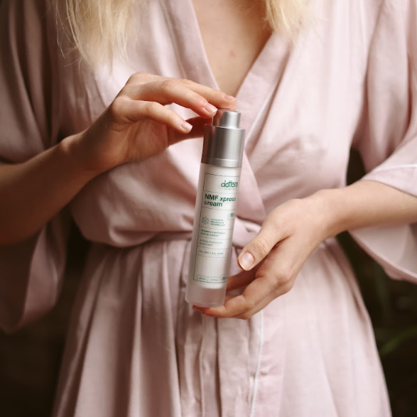 Kobieta w szlafroku trzymająca buteleczkę z nawilżającym kremem do twarzy podczas wieczornej rutyny.