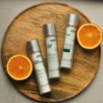 Serum i kremy z witaminą C oraz retinolem ułożone na drewnianej tacy z plastrami pomarańczy.