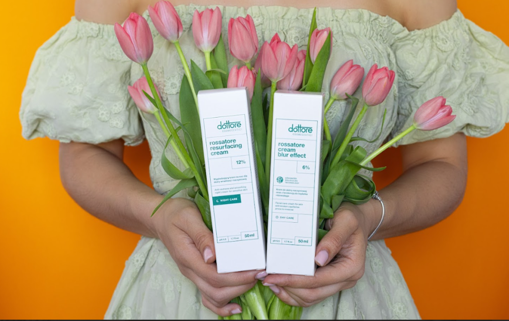 Kobieta trzymająca pudełka z kremami przeciwzmarszczkowymi na tle bukietu różowych tulipanów.
