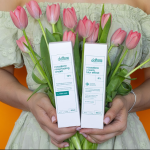 Kobieta trzymająca pudełka z kremami przeciwzmarszczkowymi na tle bukietu różowych tulipanów.